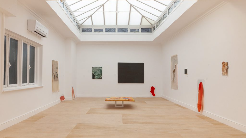 An exhibition hall with red and orange glass panels, artwork on the walls, and a horizontal piece in the center.
