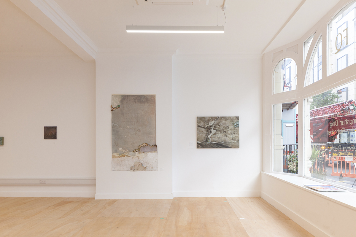 A panoramic view of a room beneath a skylight, with artwork on the walls and panels of colored glass resting on the floor.