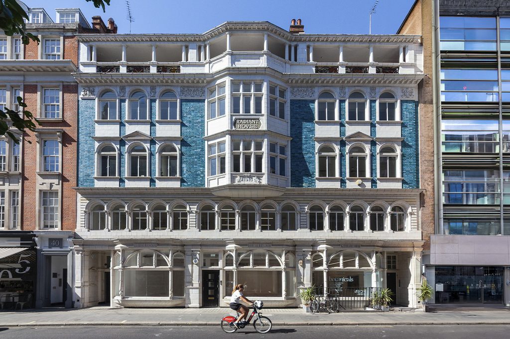 The facade of Radiant House, with blue tiles and arched windows, as a person rides by on a bicycle.