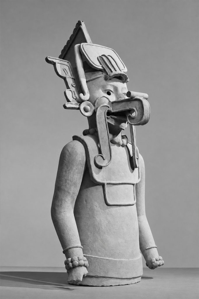 Escultura de cerámica de Ehécatl, con un elaborado tocado y una máscara bucal, fotografiada en blanco y negro.