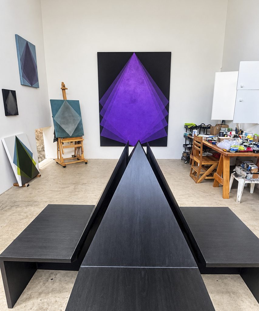 A wooden table with a gold-colored surface under an open canopy and a red-and-black geometric painting in the background.