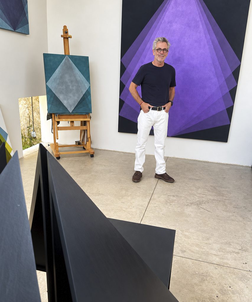 Gonzalo Lebrija in his studio in Guadalajara, standing behind a black sculpture and next to geometric paintings.