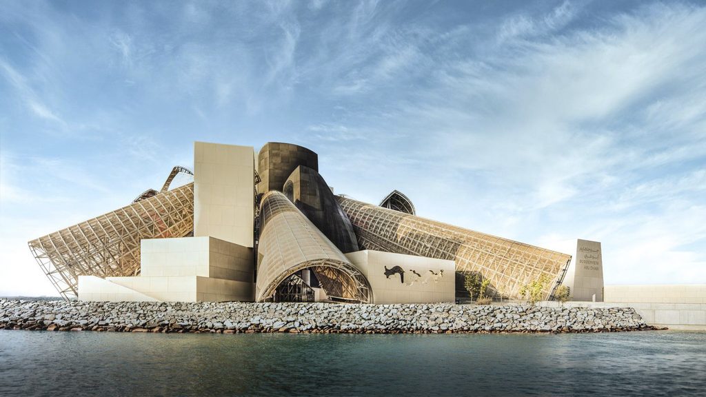 Vista del Guggenheim Abu Dhabi desde el agua, con grandes conos inclinados y una escollera al pie del edificio.