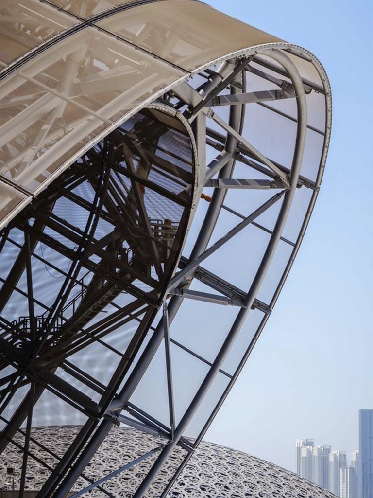Primer plano de una estructura cónica del Guggenheim Abu Dhabi, con entramado metálico y edificios al fondo.