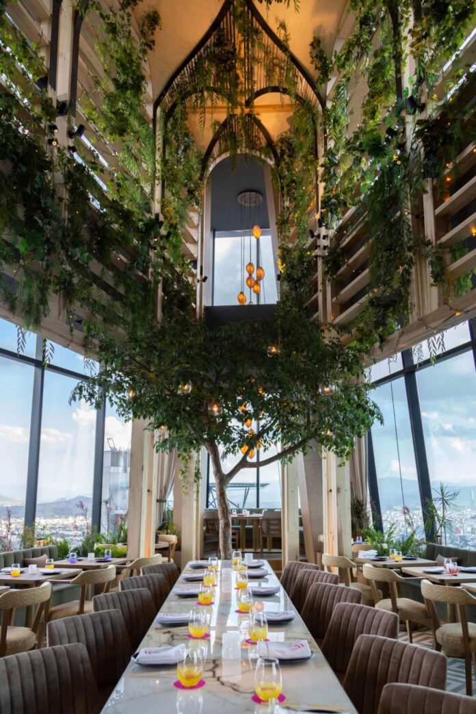 Atrio de Ling Ling México: mesa larga bajo plantas colgantes y ventanas hacia la ciudad.