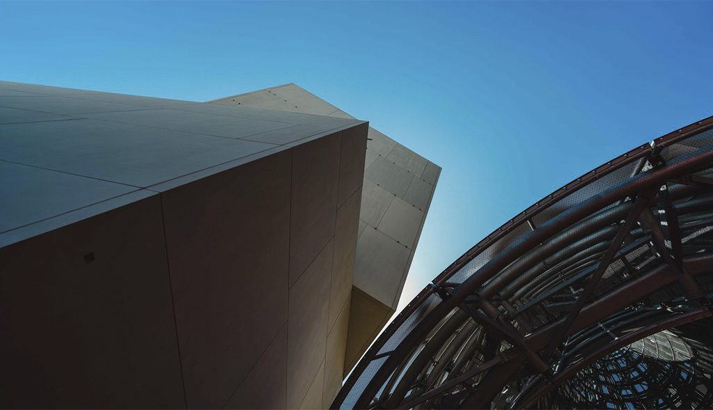 Vista desde abajo de un volumen angular claro junto a una estructura metálica curva del Guggenheim Abu Dhabi.