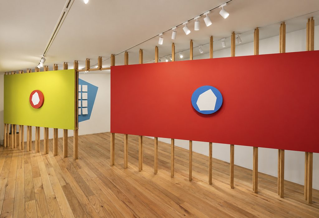 Vista de la exposición Momentum con paneles rojo y verde amarillo sostenidos por listones de madera, y pinturas circulares con polígonos claros en el centro.