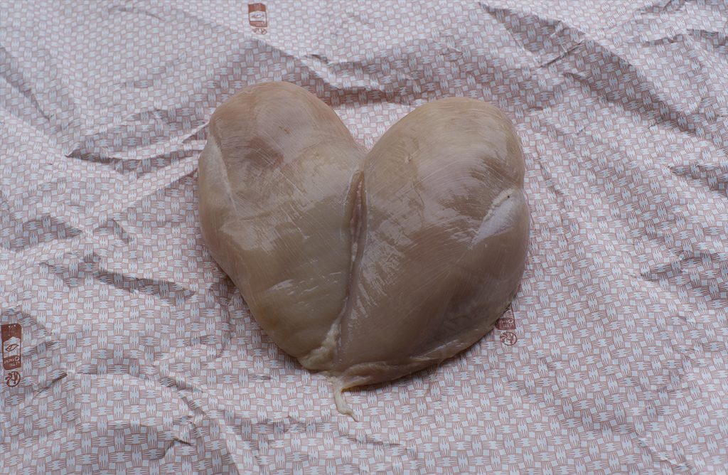 Dos piezas de carne cruda colocadas juntas en forma de corazón sobre una superficie de papel estampado en rojo y blanco.
